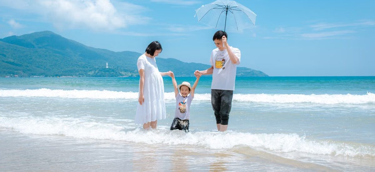 Happy family enjoying a sunny day at Da Nang Beach, Vietnam, playing in the waves.